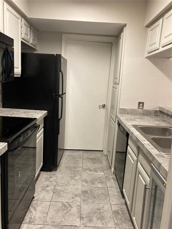 18240 Midway Road, Unit 905 Dallas, TX 75287 - Photo 6 of 15 Kitchen with black appliances, white cabinetry, and tile countertops