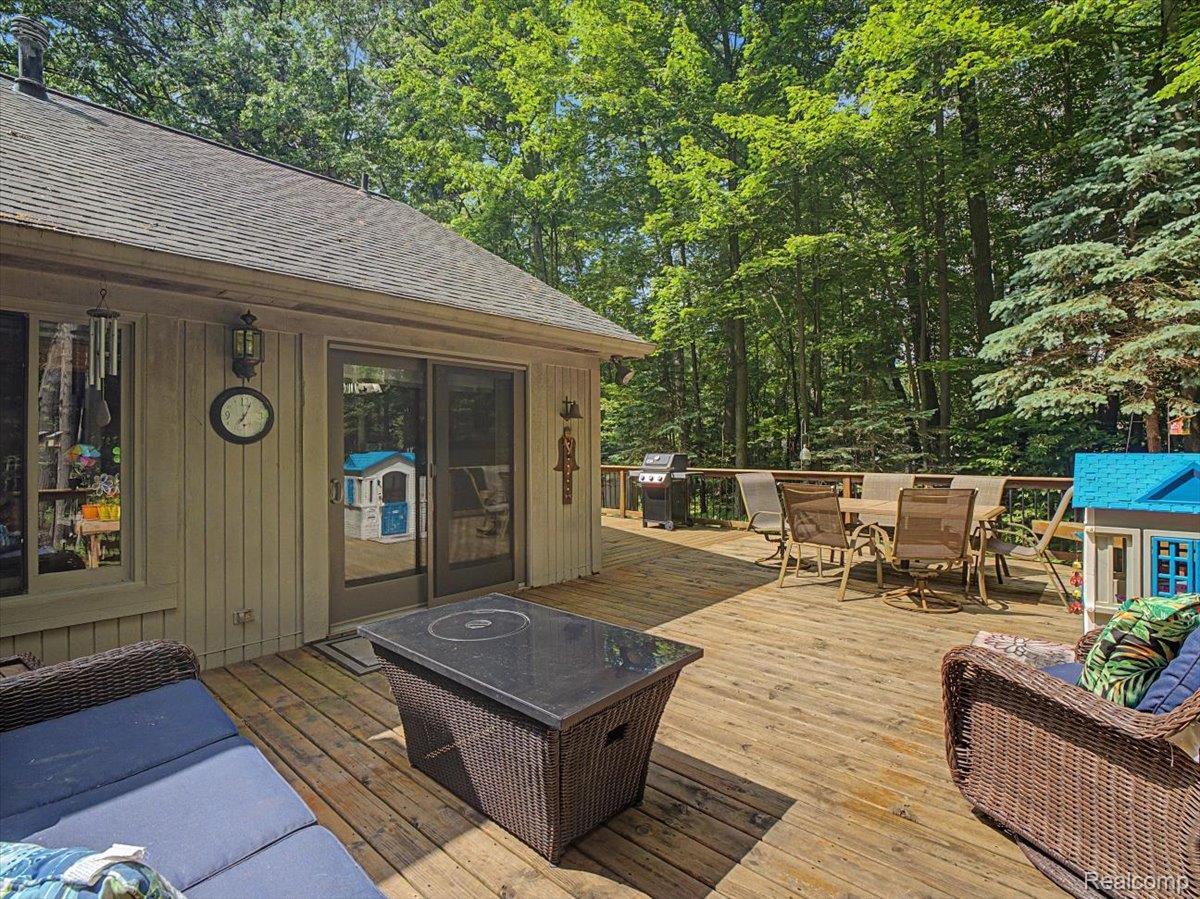 9714 Naiad Road Clarkston, MI 48348 - Photo 9 of 61 Spacious outdoor wood deck featuring a sliding glass door for interior access and a natural tree-lined backdrop.