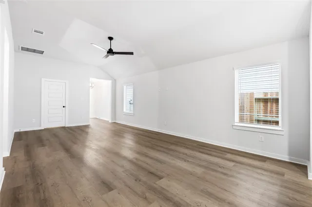an empty room with wooden floor ceiling fan and windows