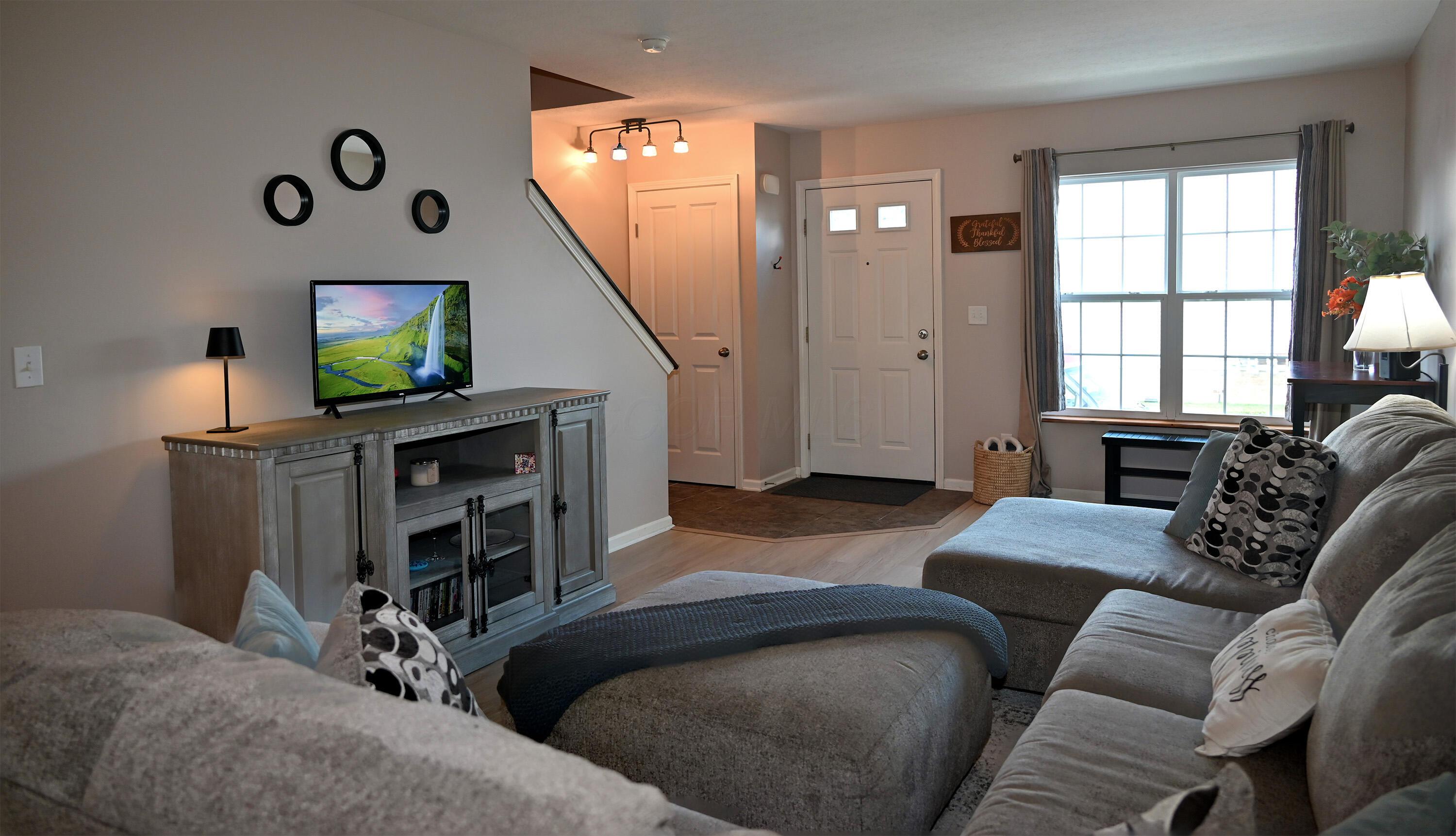 8289 Bruntsfield Road Columbus, OH 43235 - Photo 5 of 36 Spacious living room featuring luxury vinyl plank flooring, abundant natural light, neutral décor, and a welcoming entry foyer with coat closet and staircase access.