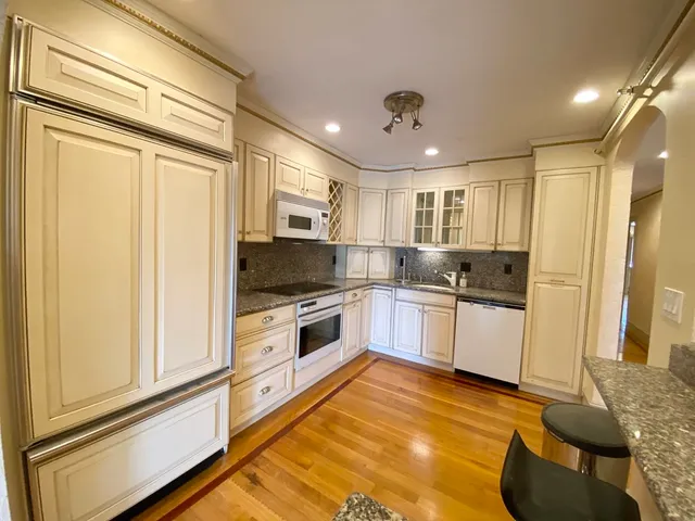 a large white kitchen with stainless steel appliances granite countertop a stove a sink and a refrigerator