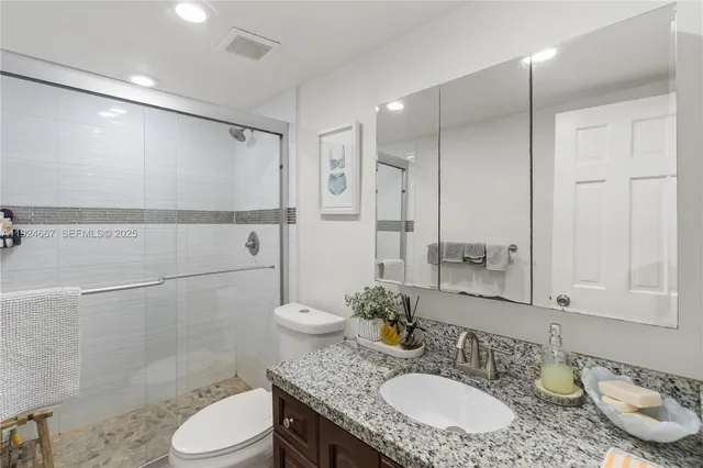 a bathroom with a granite countertop sink a toilet a mirror and shower