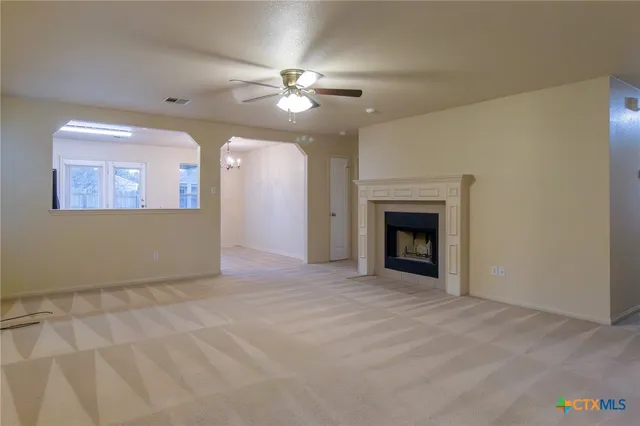 a view of an empty room with chandelier fan and fire place