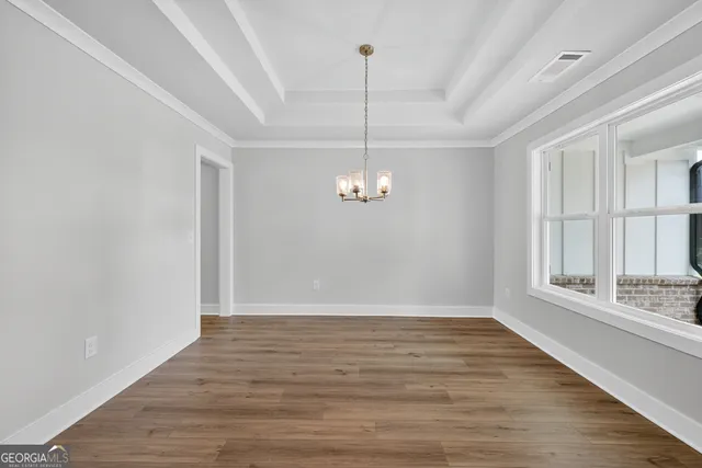 a view of an empty room with wooden floor kitchen view and a window