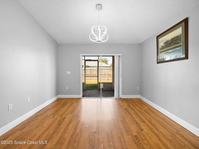 a view of an empty room with wooden floor and fan