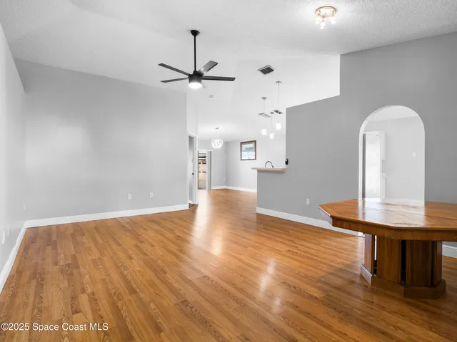 a view of a room with wooden floor a ceiling fan and kitchen space