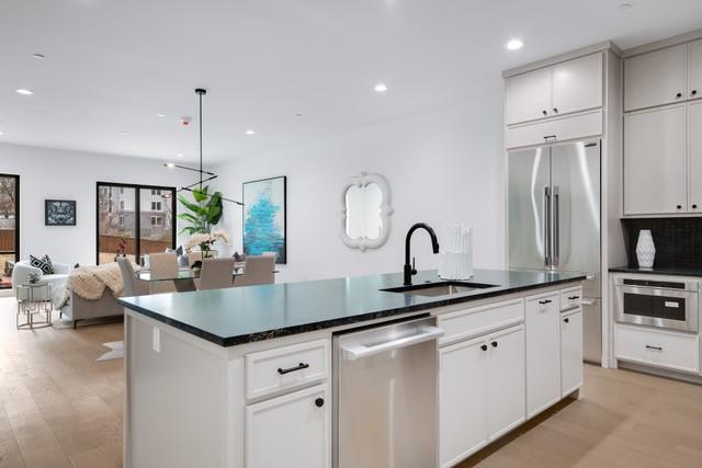 3601 Routh Street, Unit 2E Dallas, TX 75219 - Photo 6 of 14 Kitchen featuring a kitchen island with sink, a sink, stainless steel appliances, and dark countertops