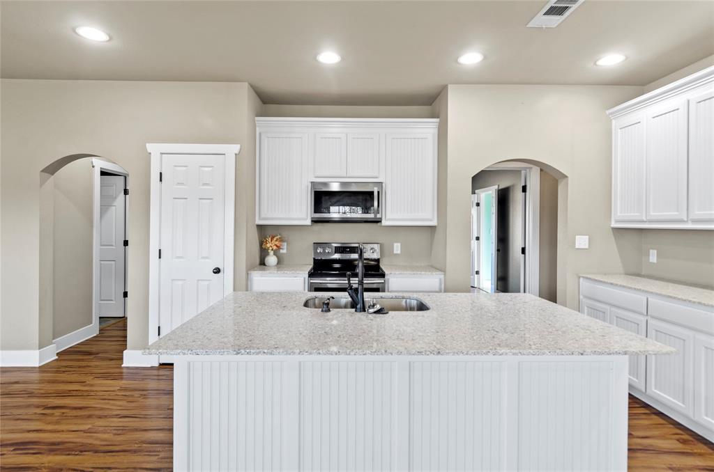 395 Yacht Club Road Oak Point, TX 75068 - Photo 22 of 23 Kitchen with arched walkways, white cabinets, light stone countertops, stainless steel appliances, and a center island with sink