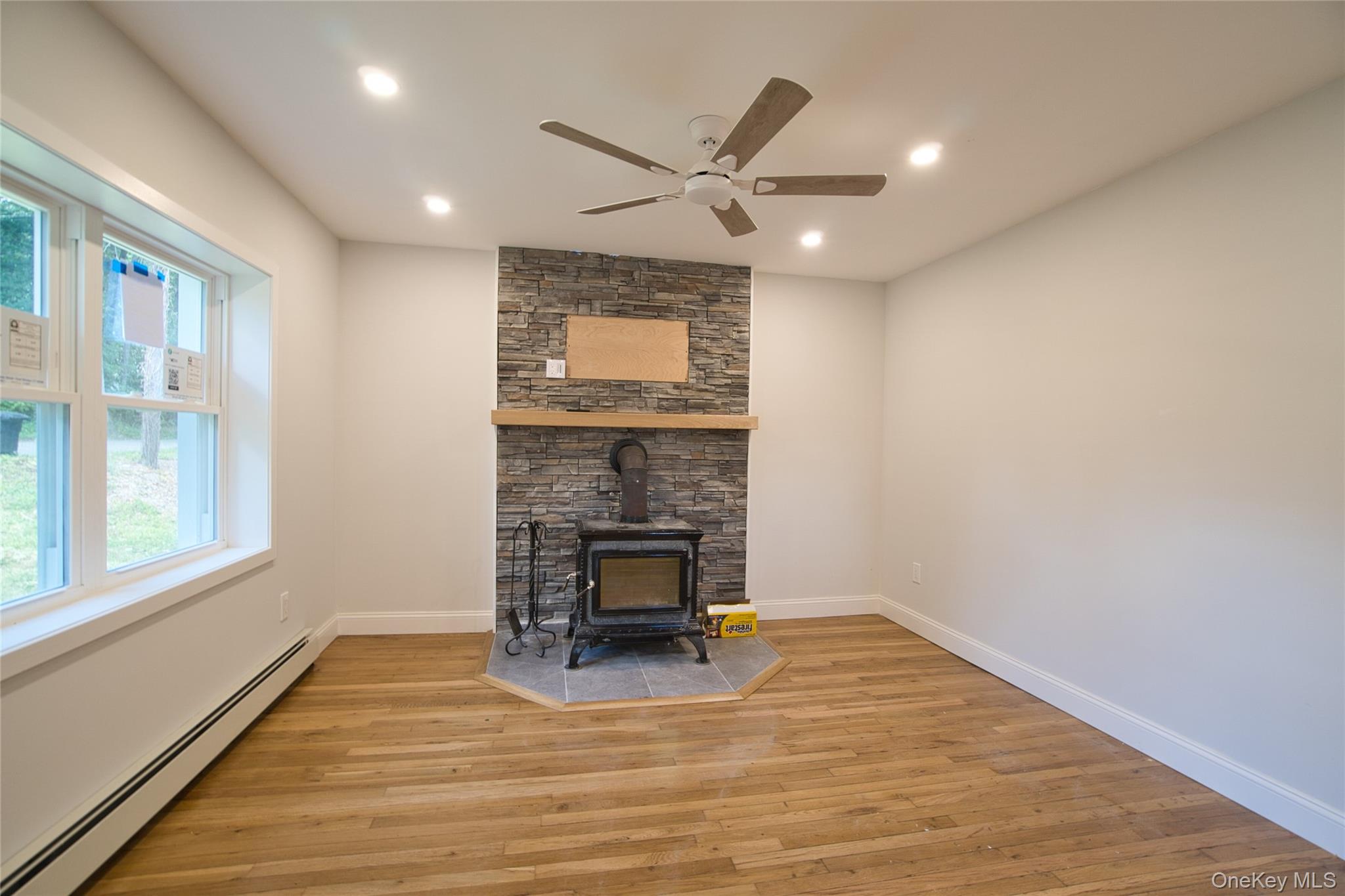 29 Overlin Road Patterson, NY 12563 - Photo 3 of 16 Living space featuring a stone-clad accent wall with wood stove, wood-finish flooring, a ceiling fan, recessed lighting, and white trim