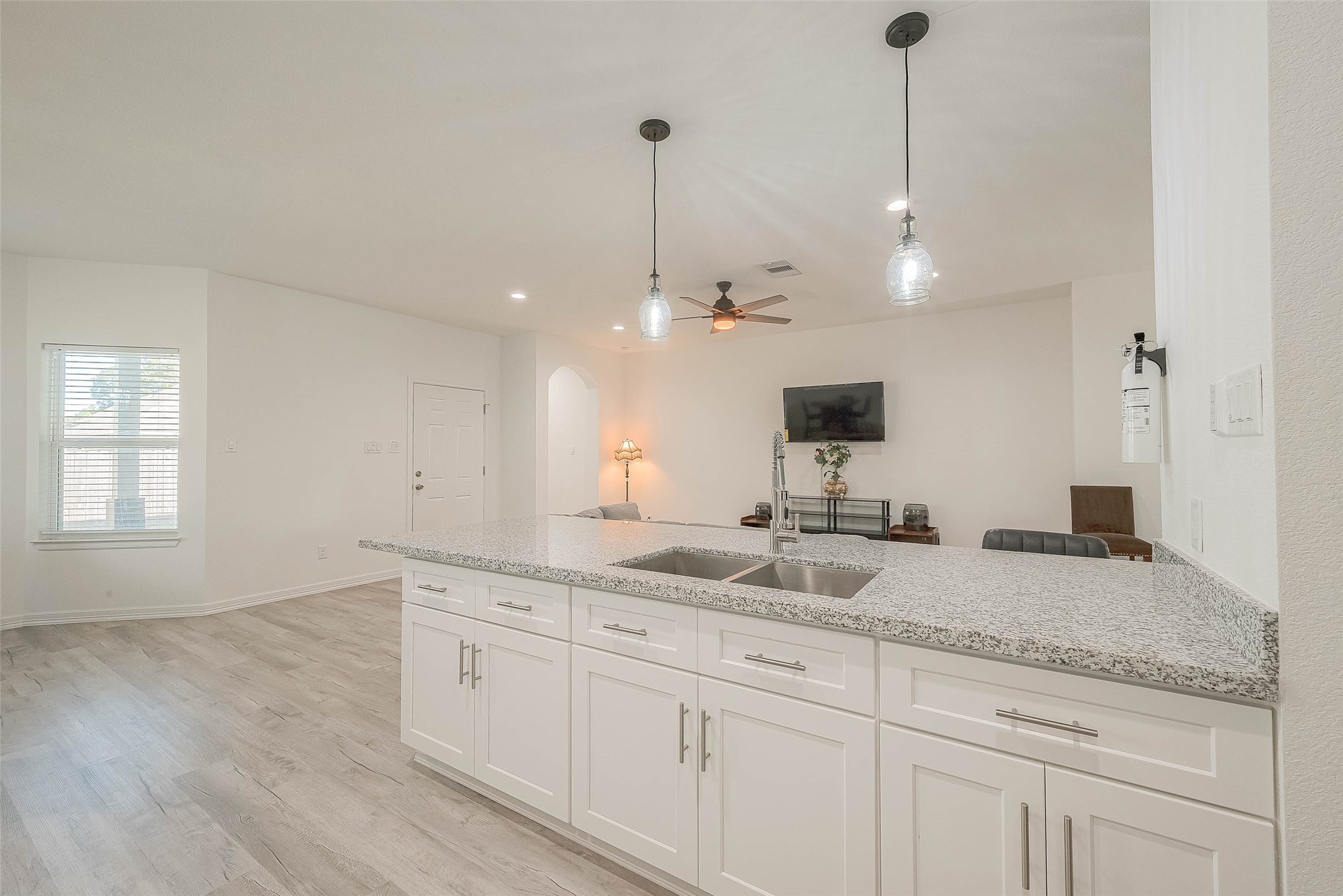 4633 Larkspur Street Houston, TX 77051 - Photo 44 of 48 This photo showcases a modern, open-concept living area with a spacious kitchen featuring a large granite island and white cabinetry. The space is well-lit with pendant and recessed lighting, has light wood flooring.