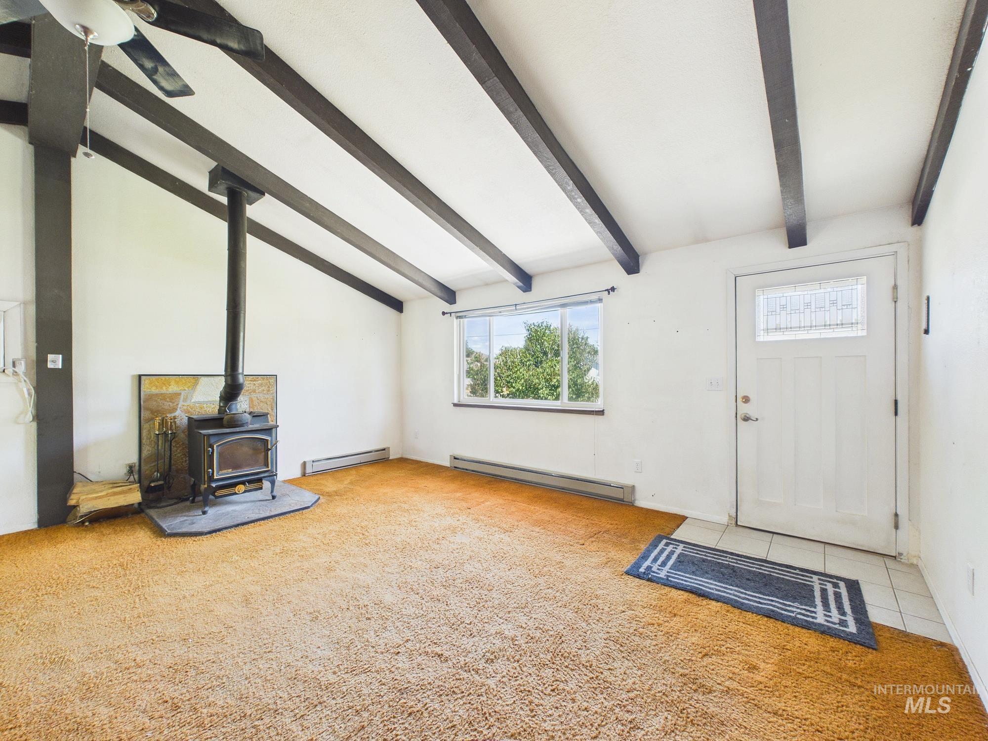 1527 North Plaza Road Emmett, ID 83617 - Photo 3 of 33 Vaulted ceiling with exposed wood beams, wood-burning stove with a hearth, and a front entry door with a decorative glass insert