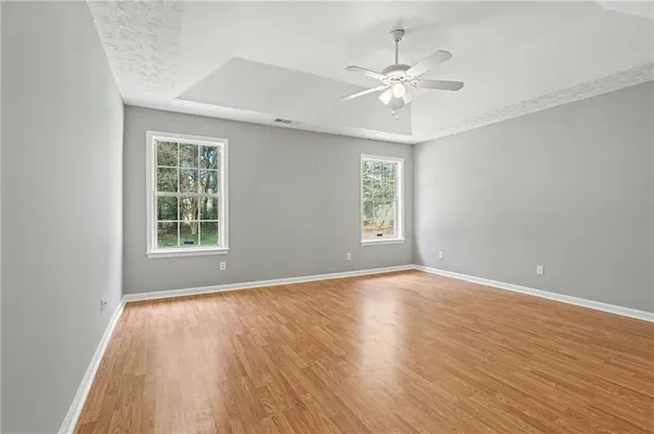an empty room with wooden floor chandelier fan and windows