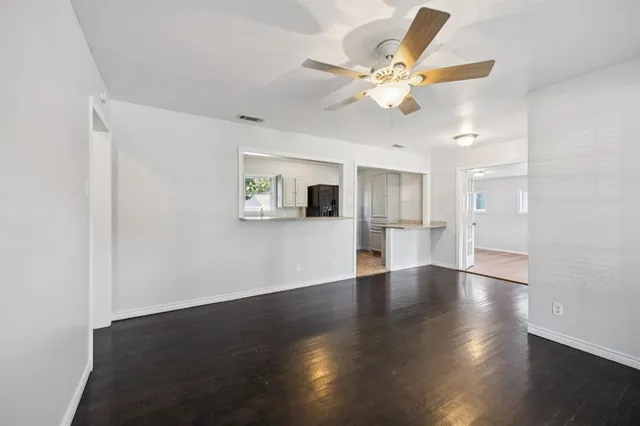 a view of an empty room with wooden floor and a ceiling fan