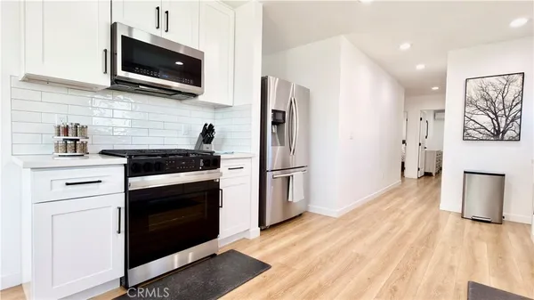 a kitchen with stainless steel appliances kitchen island granite countertop a refrigerator a stove oven a sink dishwasher and white cabinets with wooden floor