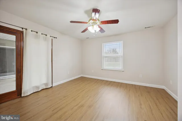an empty room with wooden floor chandelier fan and windows