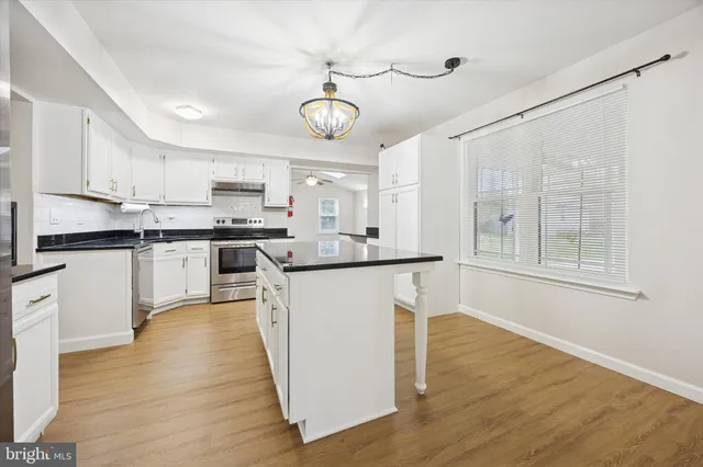 a kitchen with stainless steel appliances granite countertop a refrigerator a stove top oven a sink dishwasher and white cabinets with wooden floor