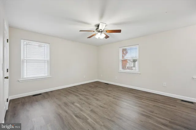 an empty room with wooden floor ceiling fan and windows