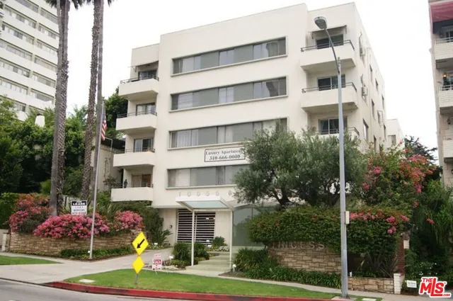 a front view of a multi story residential apartment building with yard and traffic signal