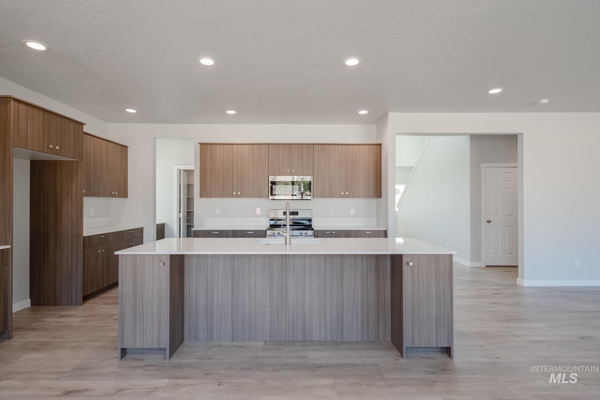 13708 Judson Street Caldwell, ID 83607 - Photo 3 of 32 Kitchen featuring modern cabinets, a kitchen island with sink, light stone counters, appliances with stainless steel finishes, and light wood-style flooring
