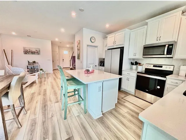 a open kitchen with stainless steel appliances kitchen island granite countertop a sink dishwasher stove top oven and refrigerator with wooden floor
