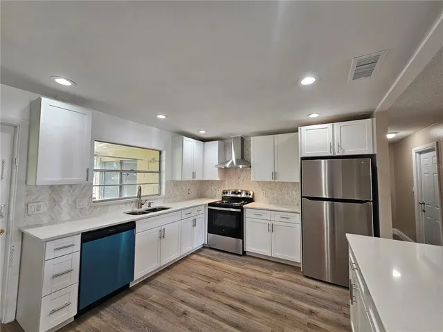 a kitchen with a white cabinets a sink a window a wooden floor and stainless steel appliances
