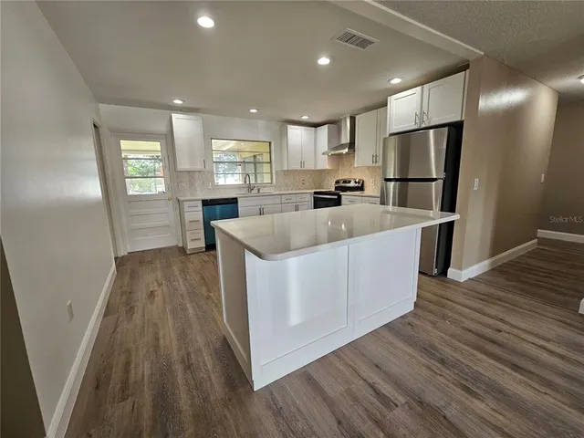 a large white kitchen with wooden floor and stainless steel appliances