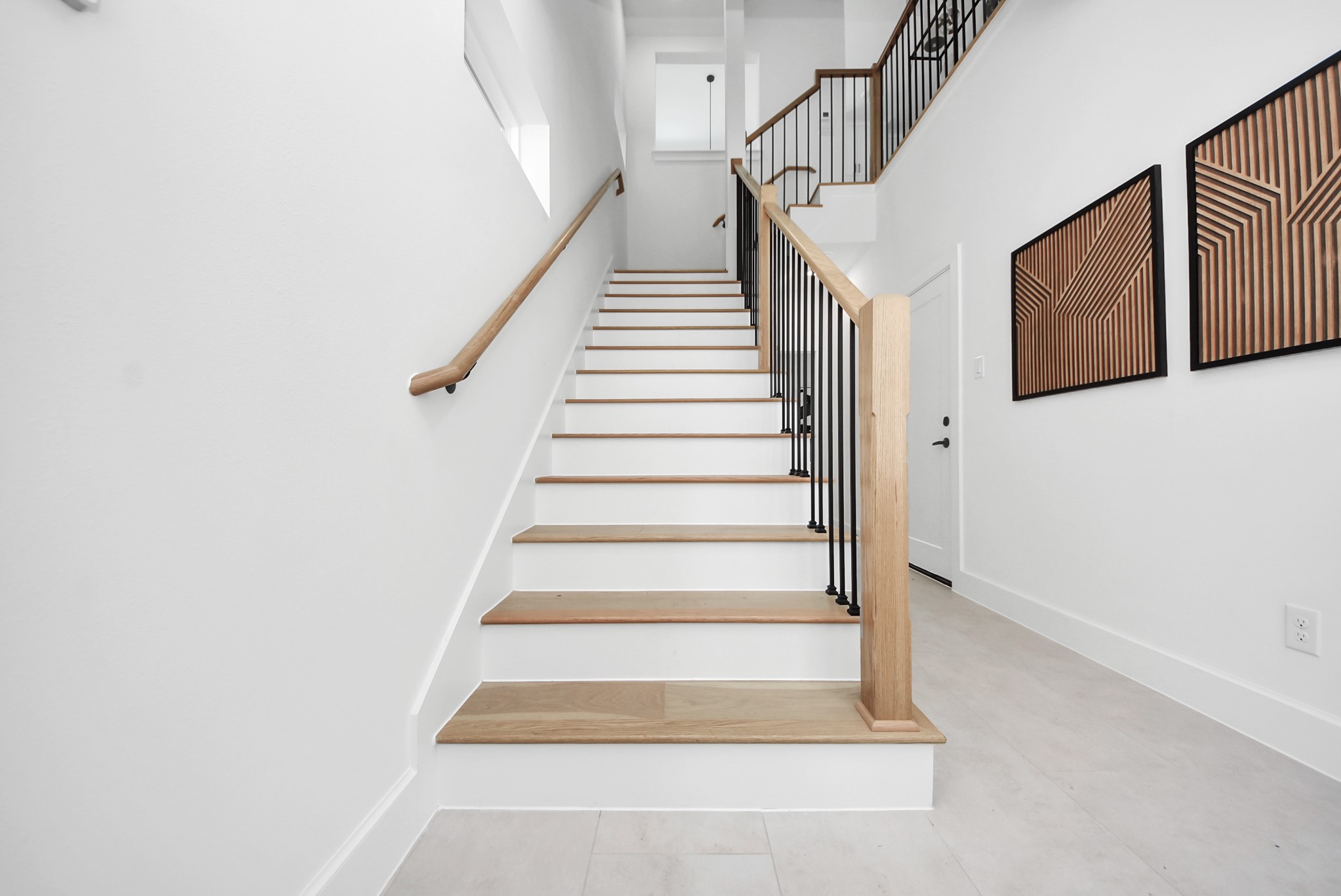 927 Fisher Street, Unit B Houston, TX 77018 - Photo 3 of 47 Ascend this modern staircase with light wood steps and sleek black metal railings, set against bright white walls. Geometric wall art adds a contemporary touch, creating an inviting transition between the home’s levels while highlighting its clean, modern design.