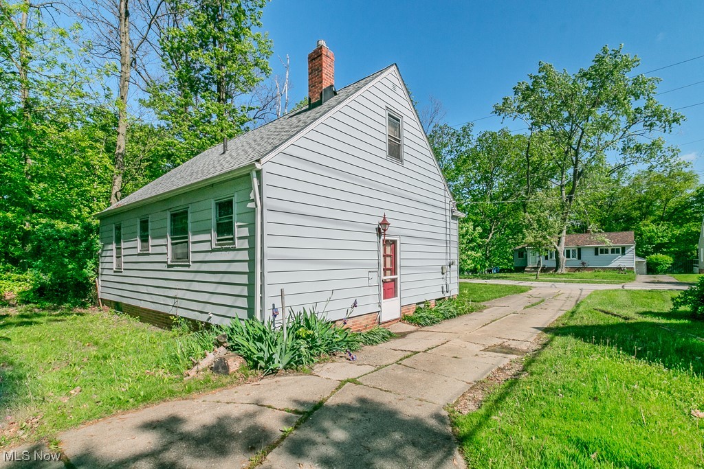 View of home's exterior featuring a chimney, a yard, and a shingled roof