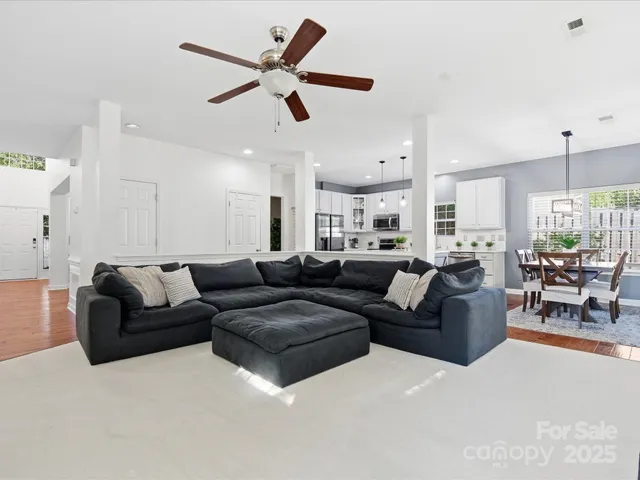 a living room with furniture kitchen area and a ceiling fan