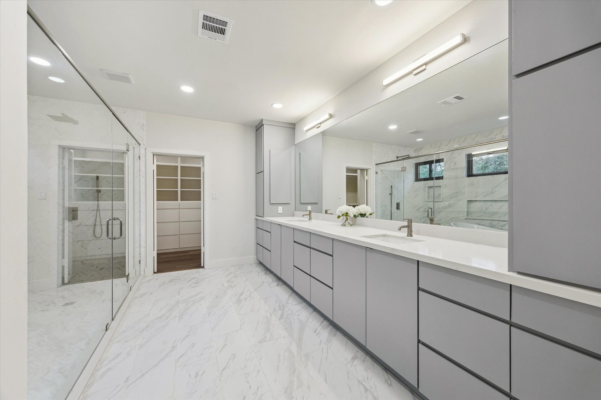 6348 Vanderbilt Street West University Place, TX 77005 - Photo 11 of 30 The primary bath is pure spa-level luxury. Stunning stone-look tile floors and floor-to-ceiling wall tile set a crisp, elegant backdrop for the freestanding soaking tub, oversized frameless glass shower with rain head, and an expansive dual-sink vanity with sleek custom cabinetry and full-length mirror. Natural light pours in through black-framed windows, and a custom walk-in closet sits just steps away. Every finish, every detail, every inch, designed to indulge.