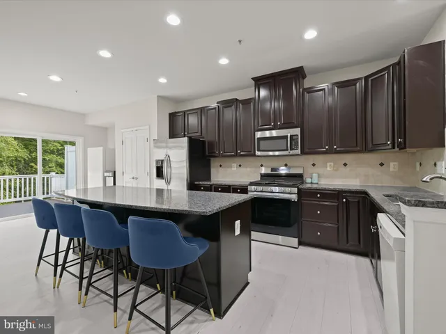 a kitchen with stainless steel appliances kitchen island granite countertop a sink a microwave a refrigerator and wooden cabinets