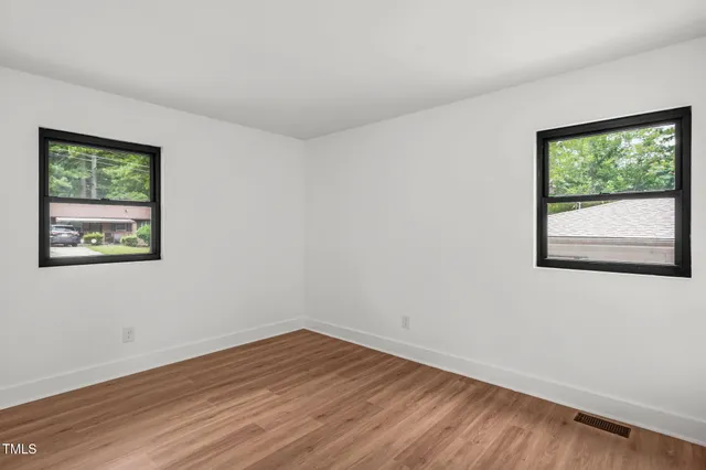 a view of an empty room with wooden floor and a window