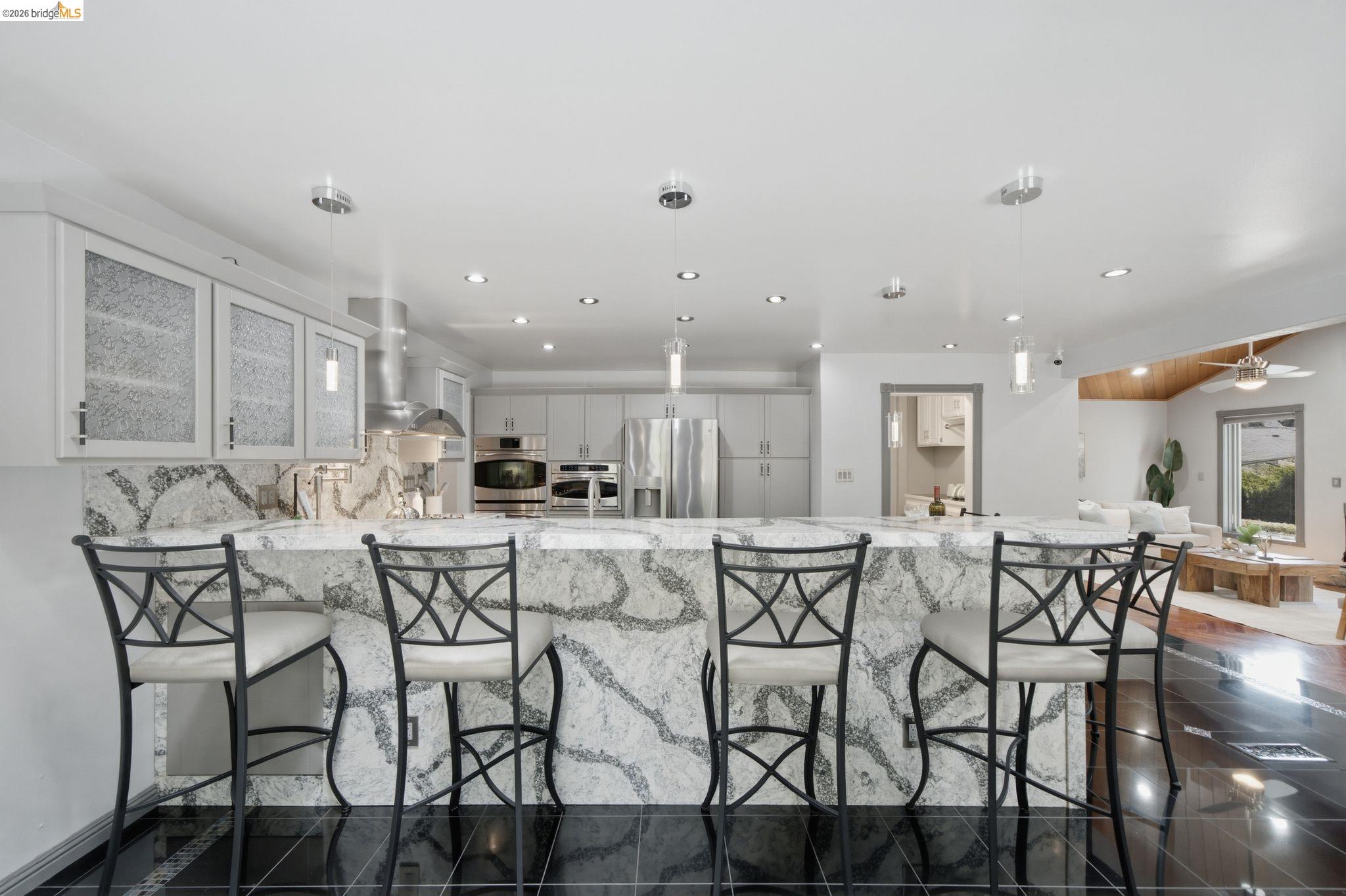 11133 Golf Links Road Oakland, CA 94605 - Photo 18 of 57 Kitchen featuring a large waterfall island with integrated seating, recessed lighting, pendant lighting, stainless steel appliances, and black tile flooring