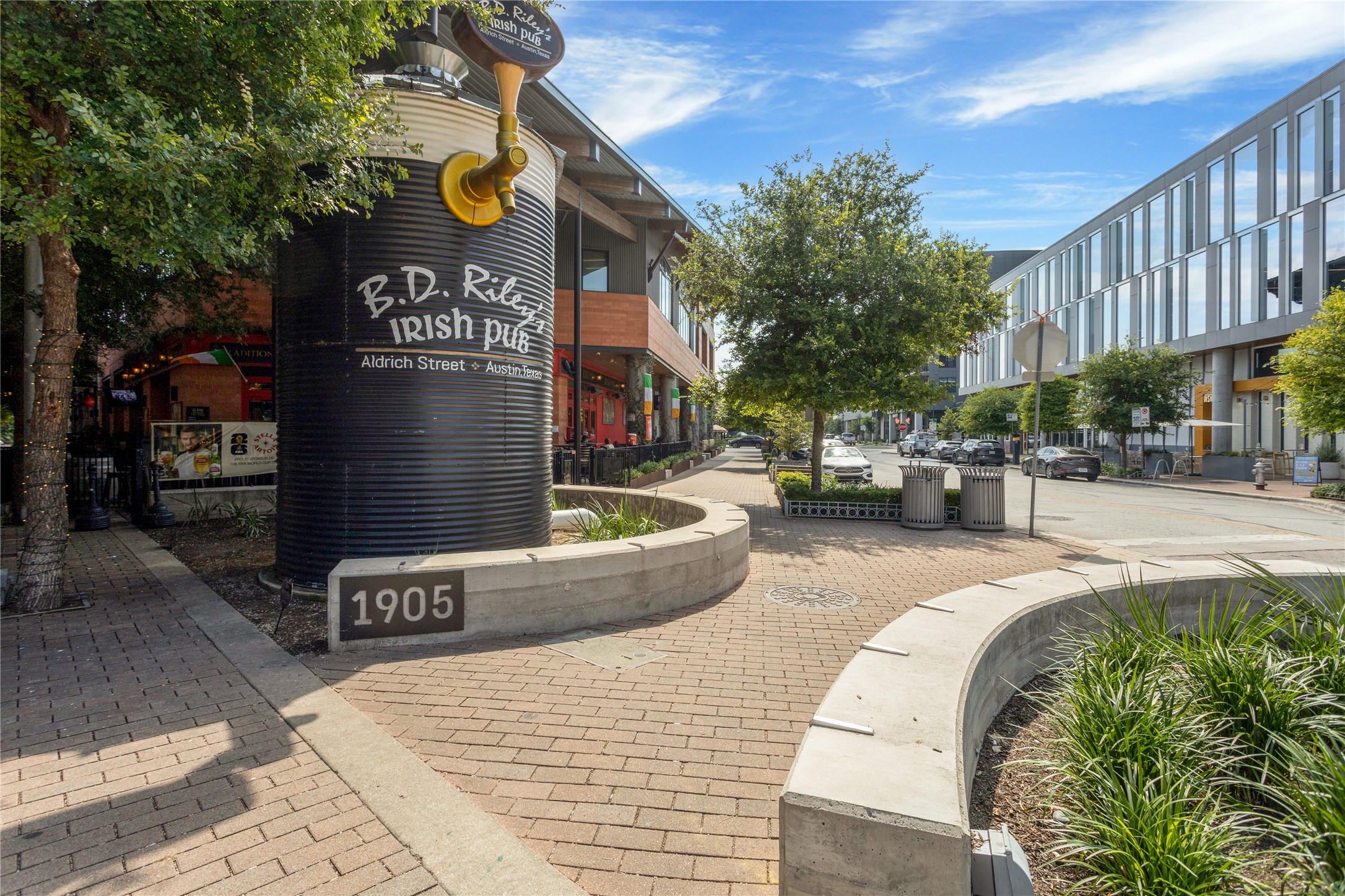 2805 McCurdy Street, Unit 14 Austin, TX 78723 - Photo 32 of 40 A vibrant commercial street showcases a distinct pub entrance and a contemporary building under a bright sky.