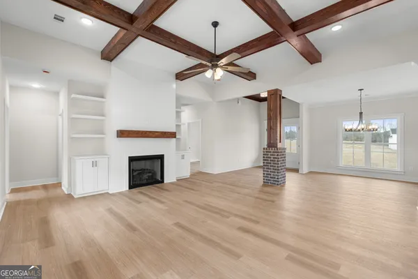 a view of an empty room with a fireplace a ceiling fan and wooden floor