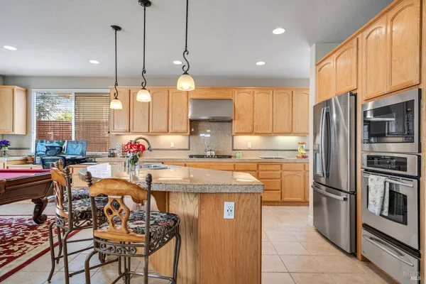 a kitchen with stainless steel appliances granite countertop a refrigerator a sink a stove and a dining table with wooden floor