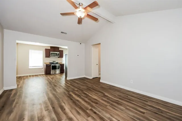 an empty room with wooden floor ceiling fan and windows