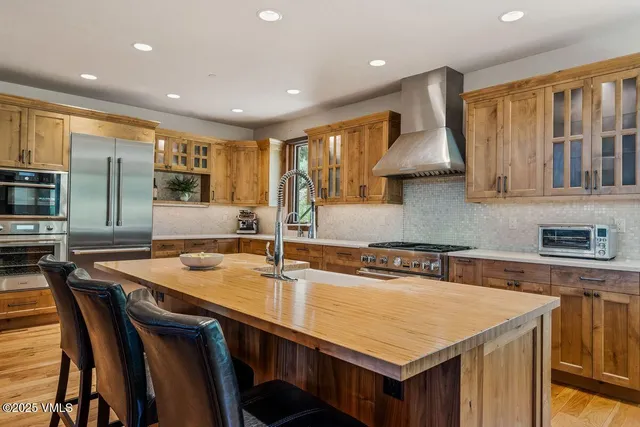 a kitchen with stainless steel appliances granite countertop a sink a stove a refrigerator cabinets and chairs
