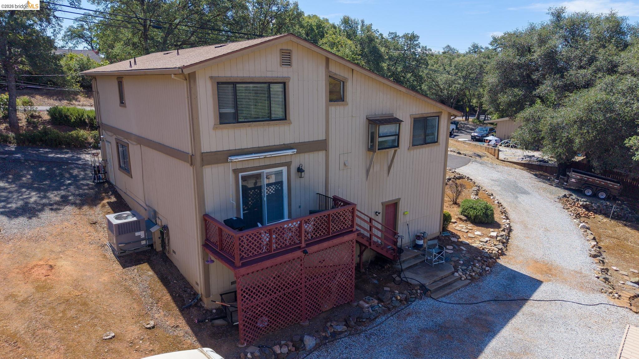 11858 Campo Seco Road Sonora, CA 95370 - Photo 3 of 45 Two-story residence featuring a ground-level deck with lattice skirting, sliding glass door access, and a gravel driveway