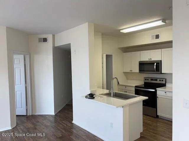 a kitchen with stainless steel appliances a stove top oven a sink a refrigerator white cabinets and wooden floor