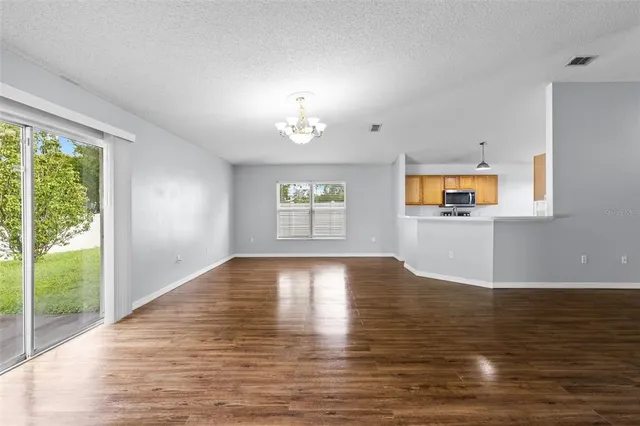 an empty room with wooden floor chandelier fan and windows