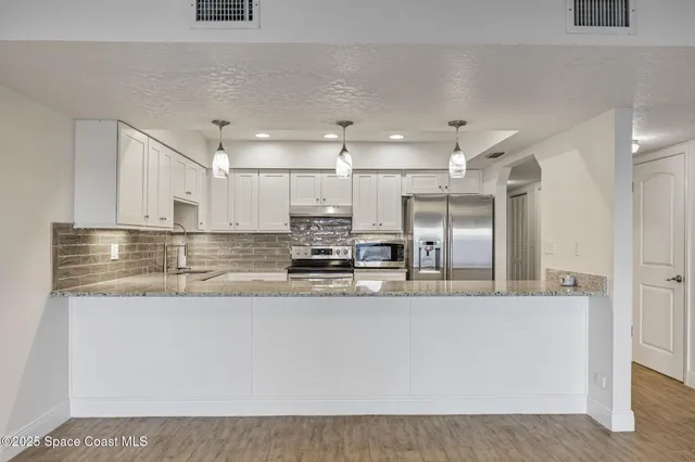 a large white kitchen with kitchen island a counter top space and stainless steel appliances