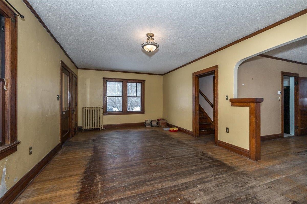 701 East 4th Street Superior, WI 54880 - Photo 3 of 16 Unfurnished living room featuring dark wood-style flooring, radiator, a textured ceiling, crown molding, and arched walkways