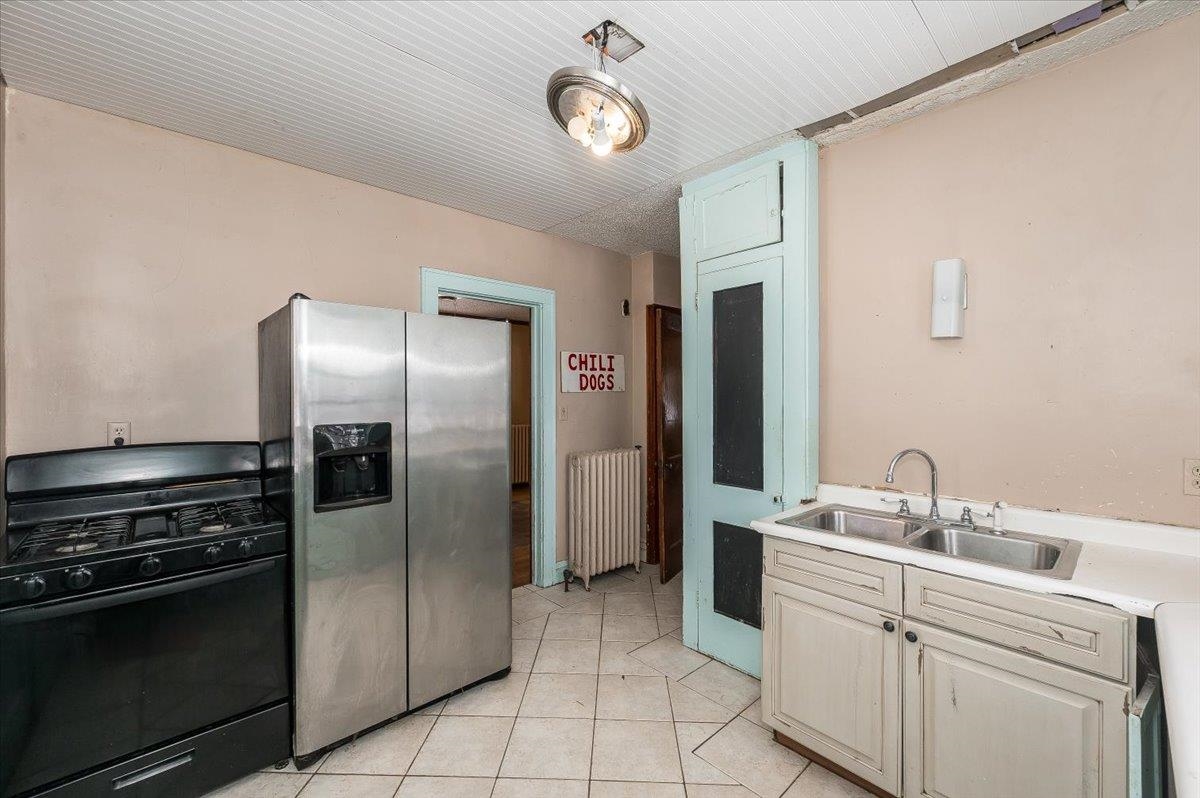 701 East 4th Street Superior, WI 54880 - Photo 6 of 16 Kitchen featuring black gas range oven, stainless steel fridge, light countertops, radiator, and light tile patterned flooring