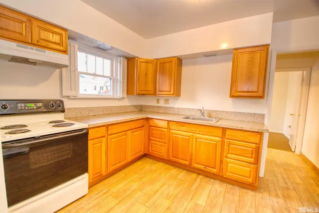 a large kitchen with granite countertop a sink a stove cabinets and wooden floor
