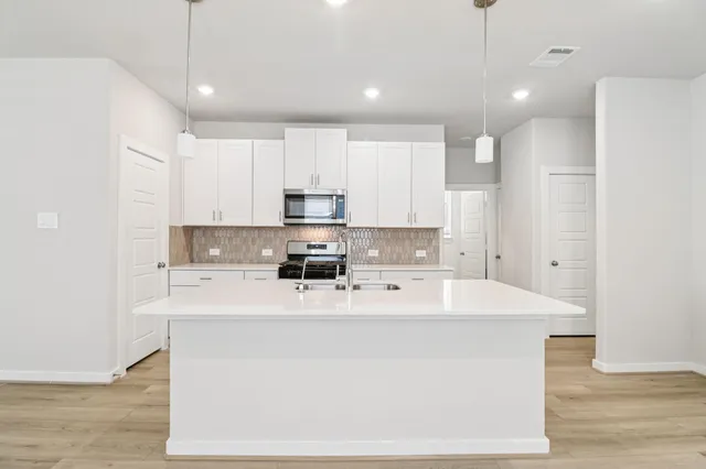 a large white kitchen with kitchen island a sink stainless steel appliances and cabinets