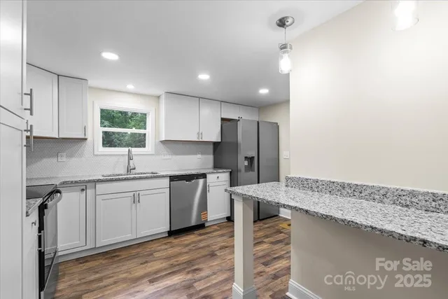 a kitchen with stainless steel appliances granite countertop a sink a stove a refrigerator and island with wooden floor