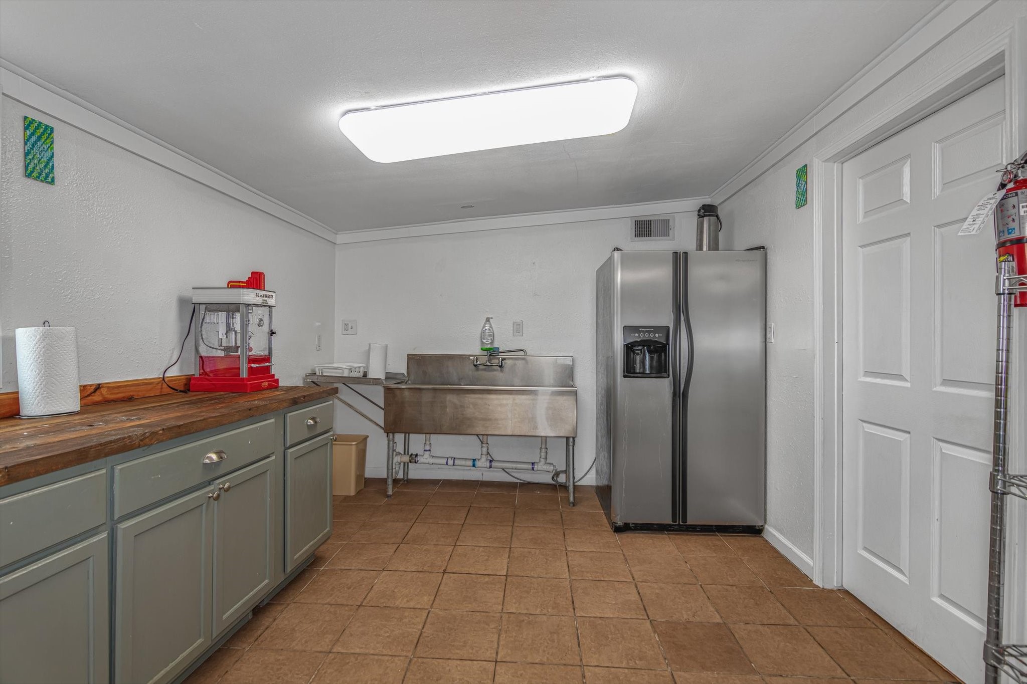 905 43rd Street Galveston, TX 77550 - Photo 20 of 43 This spacious utility room features tiled flooring, a large stainless steel sink, ample cabinetry with a wooden countertop, and a modern stainless steel refrigerator.