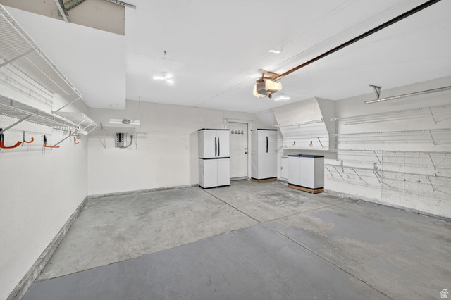 1464 990 West Provo, UT 84601 - Photo 32 of 41 Spacious garage featuring a concrete floor, overhead wire shelving, wall-mounted storage hooks, built-in storage cabinets, and a side access door