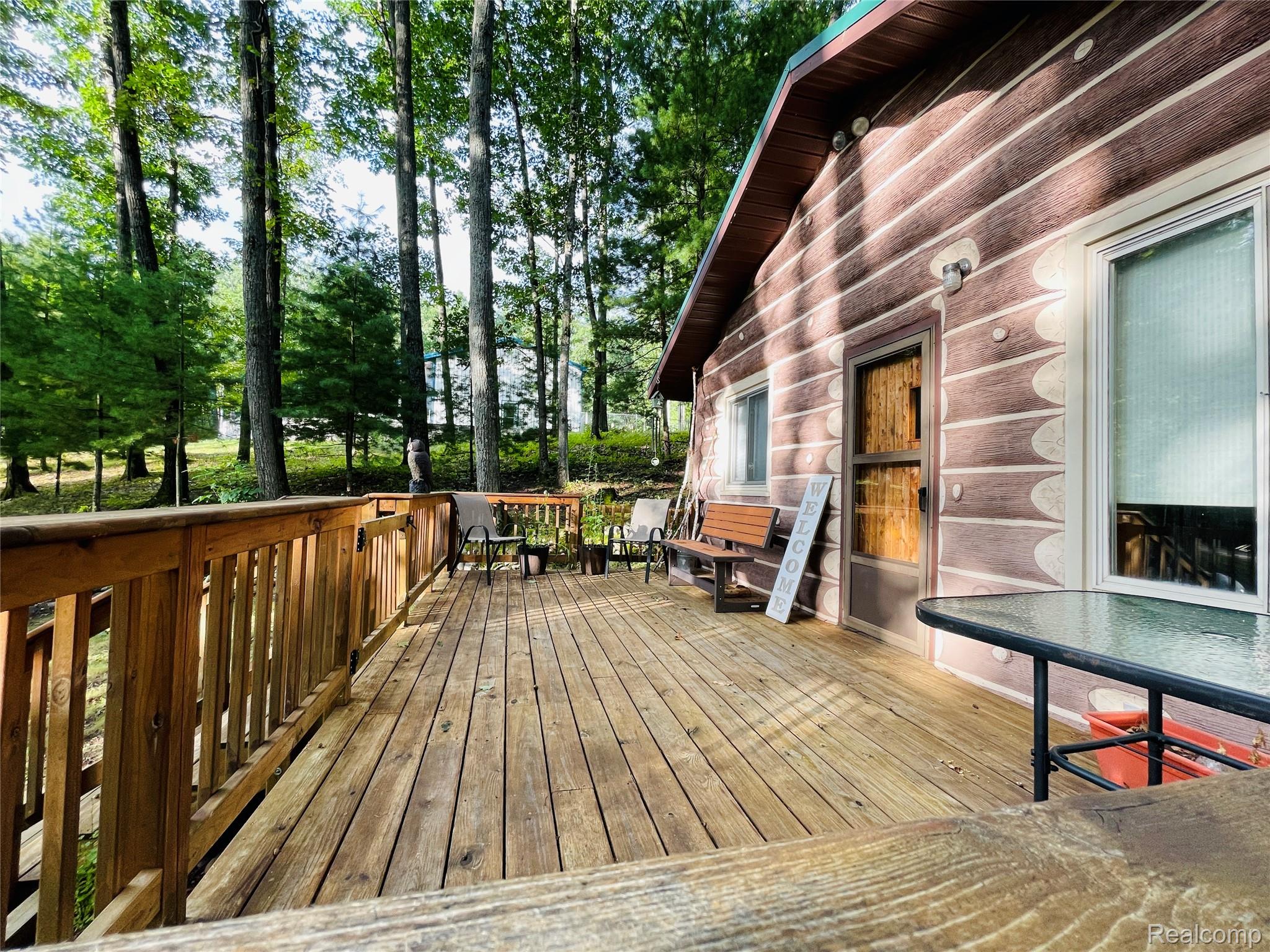 417 Ogemaw Road Rose City, MI 48654 - Photo 22 of 26 Expansive wood-finish deck with wood railing, log-style exterior siding, and dense surrounding trees
